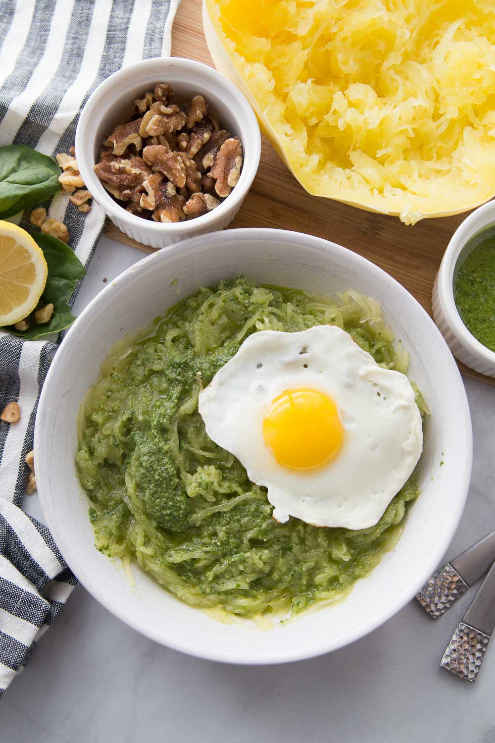 A white bowl of spaghetti squash with pesto and a fried egg