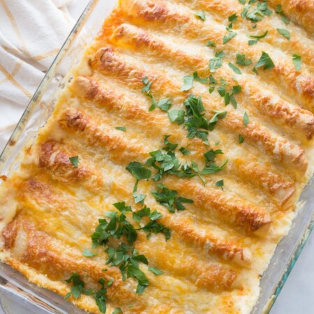 A pan full of white chicken enchiladas topped with cheese