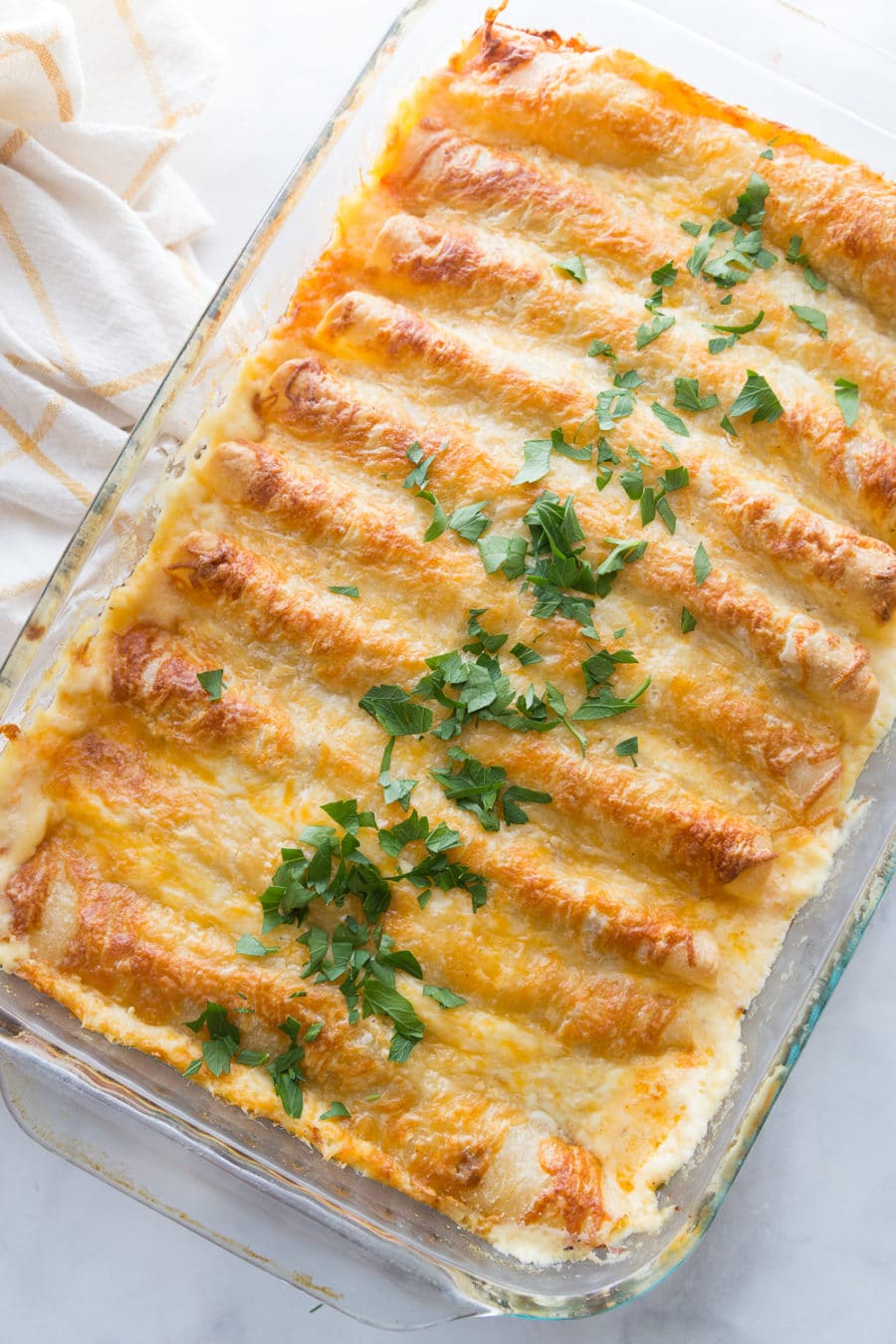 A pan full of white chicken enchiladas topped with cheese