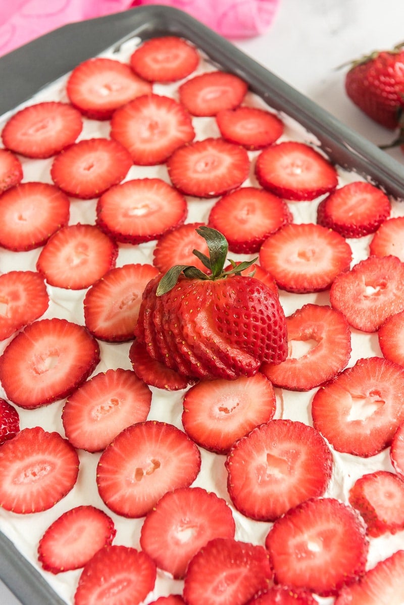 Sliced strawberries on top of a strawberry poke cake