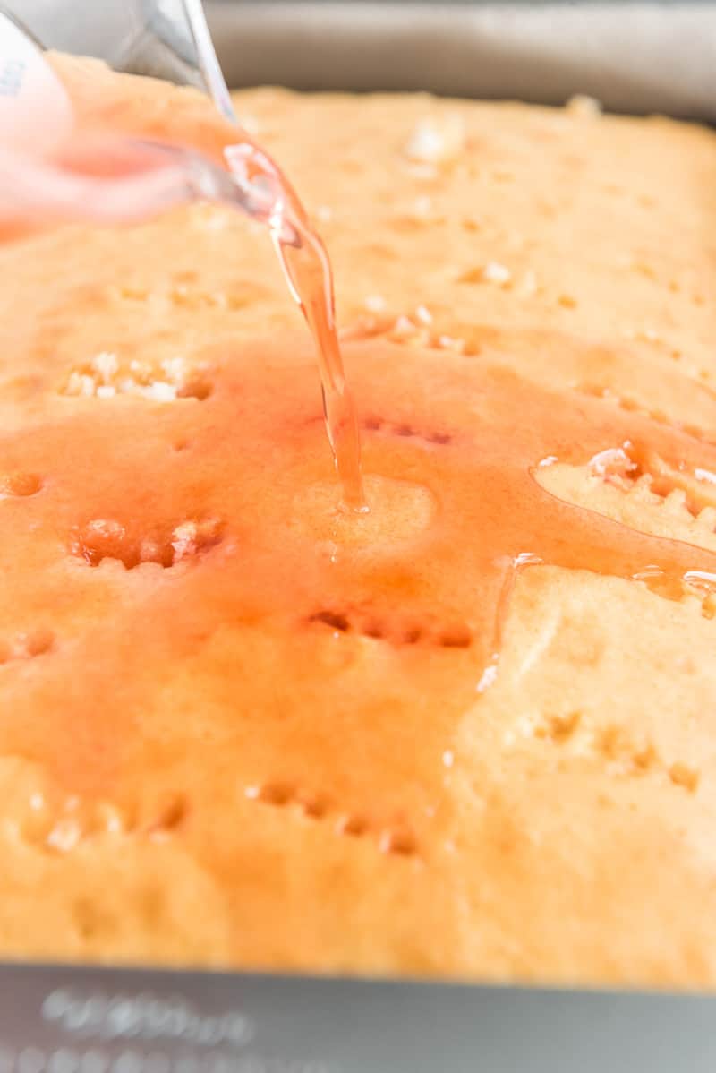 Pouring simple syrup on a strawberry poke cake