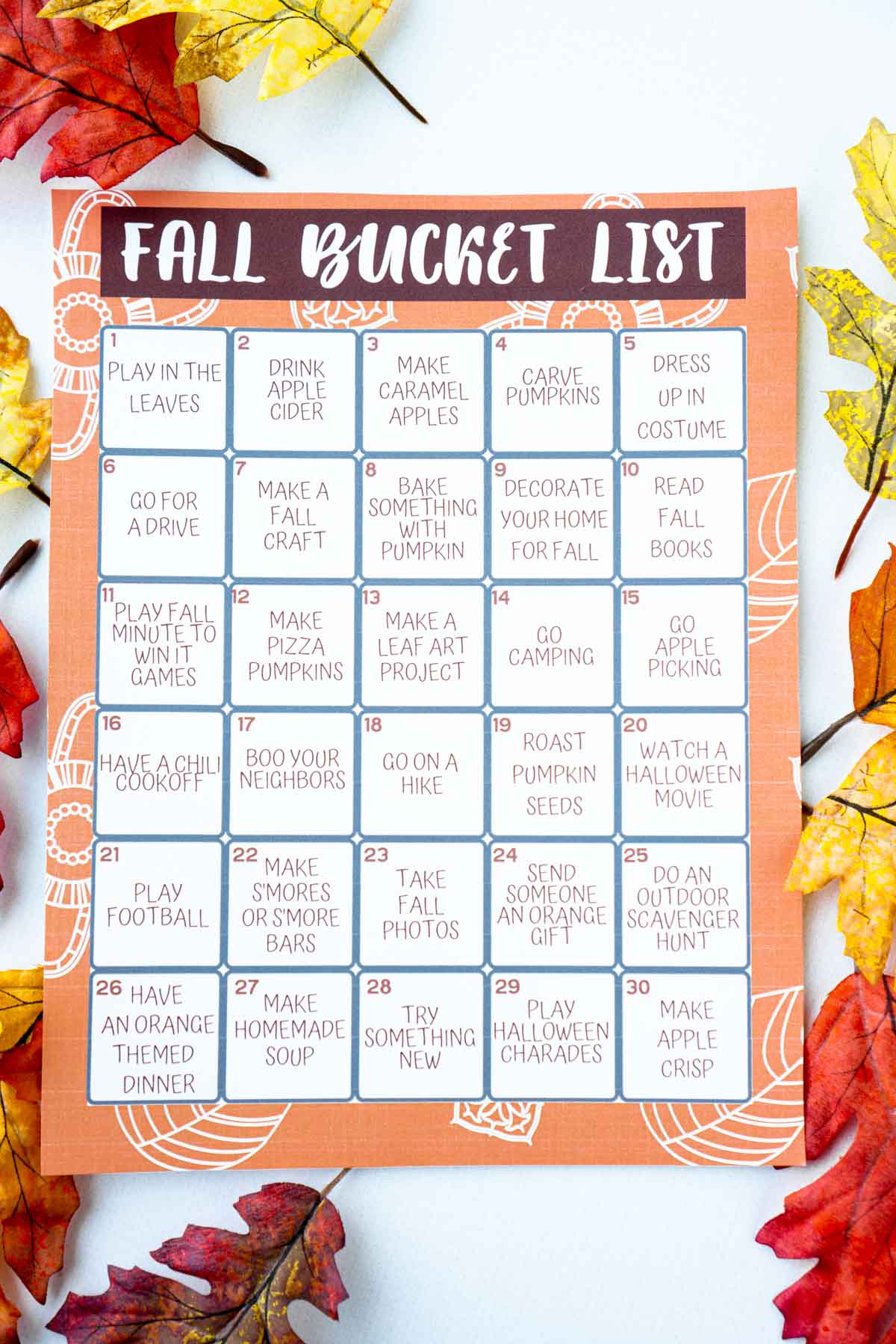 A fall bucket list calendar on top of a bunch of fall colored fake leaves