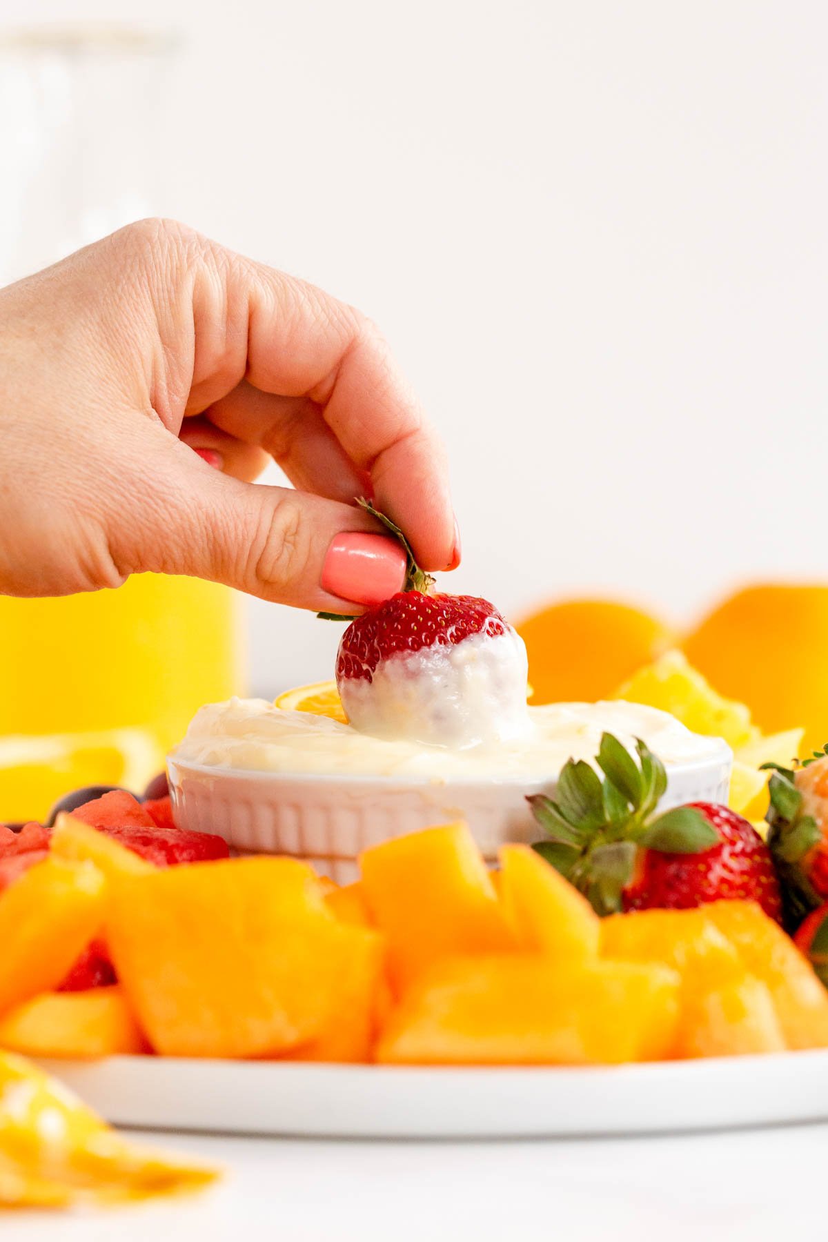 a hand dipping a strawberry in a fruit dip