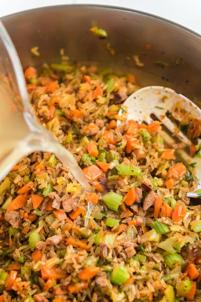 Adding broth to sausage jambalaya