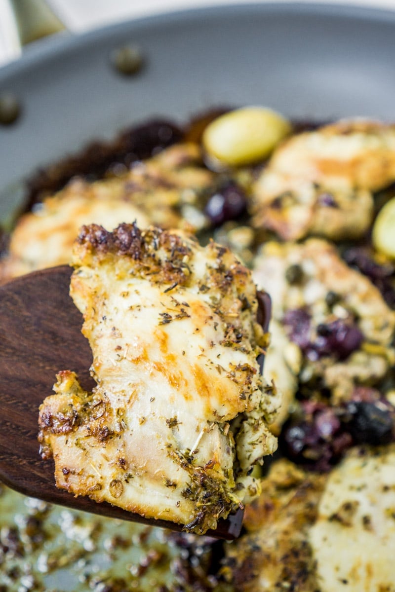 A small piece of lemon chicken above a pan full of Greek lemon chicken