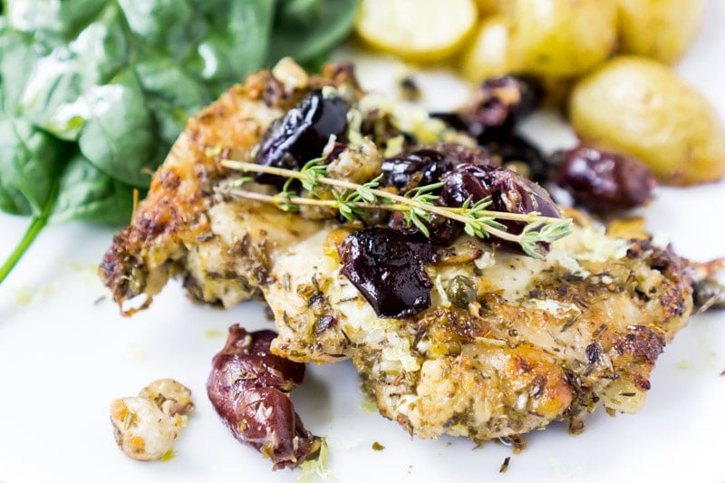 A piece of baked lemon chicken with olives and rosemary on top