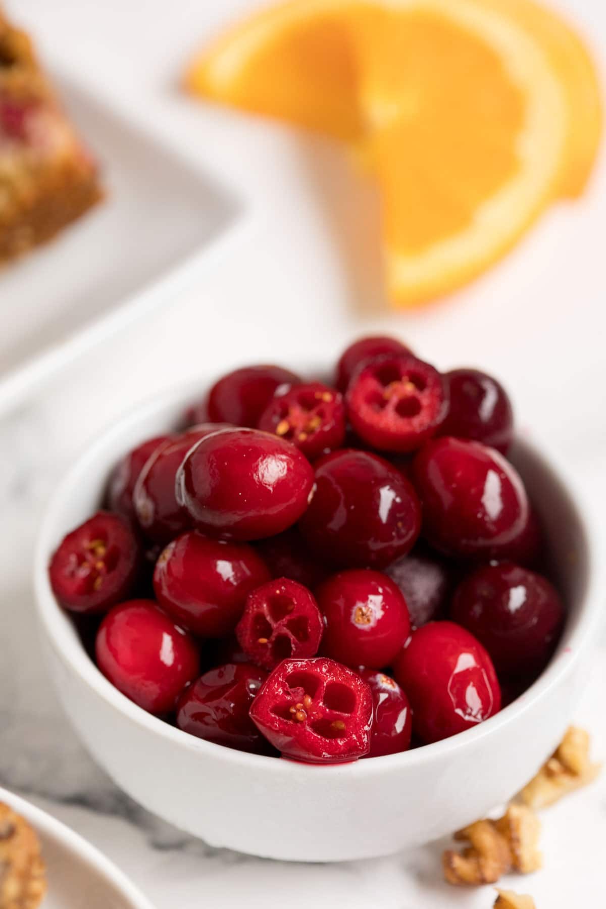 A bowl of chopped cranberries with an orange in the background