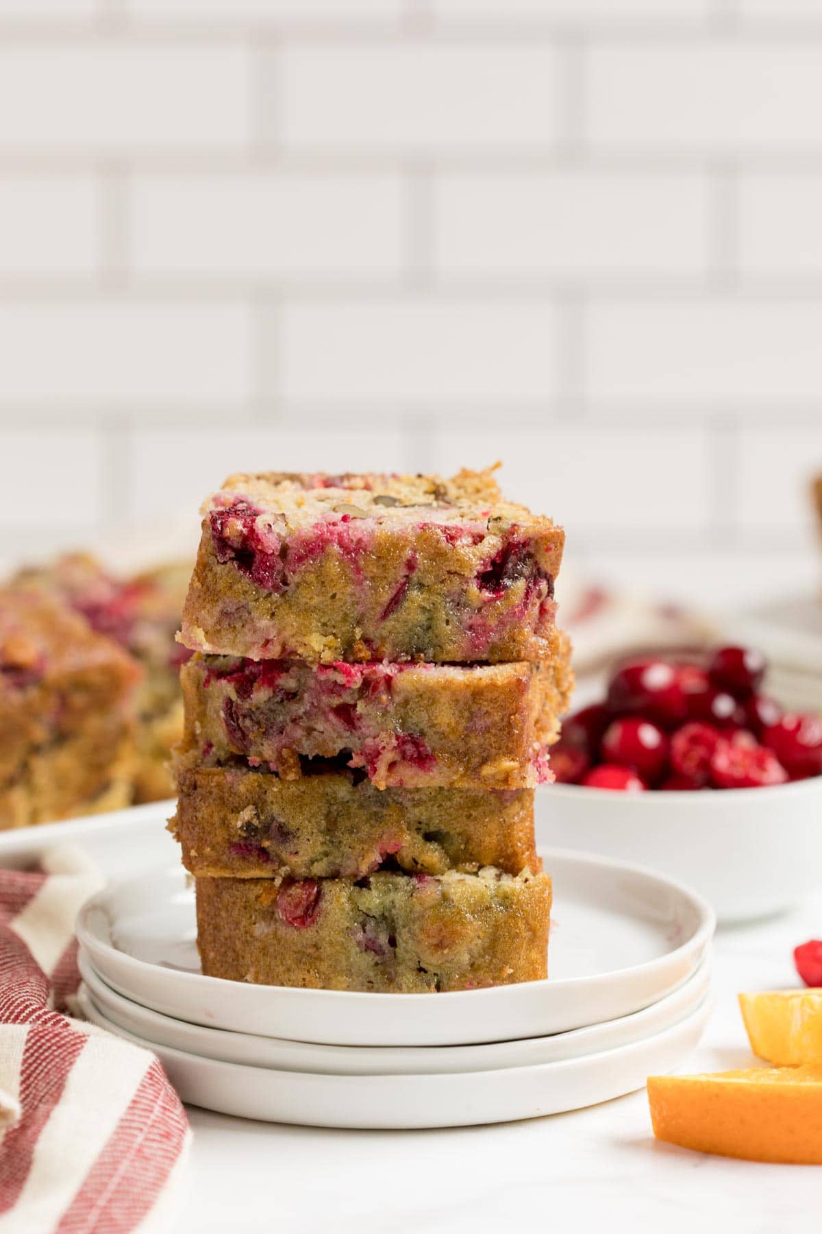 Sliced pieces of cranberry orange bread on a stack of white plates