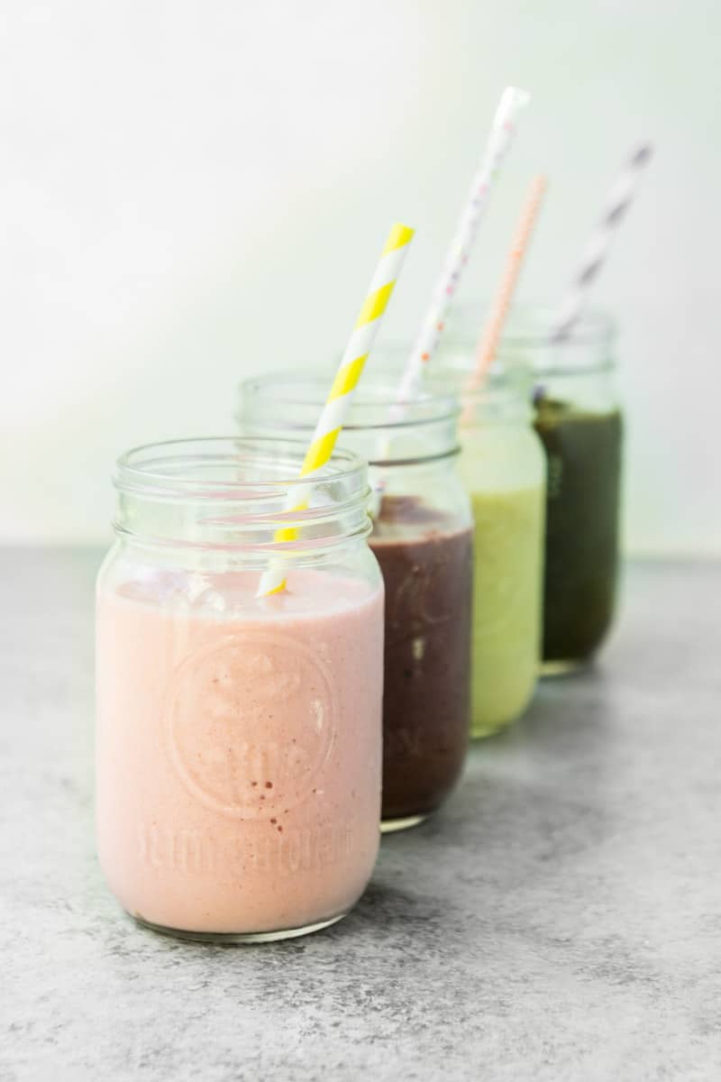 Four healthy smoothies lined up in cups with straws