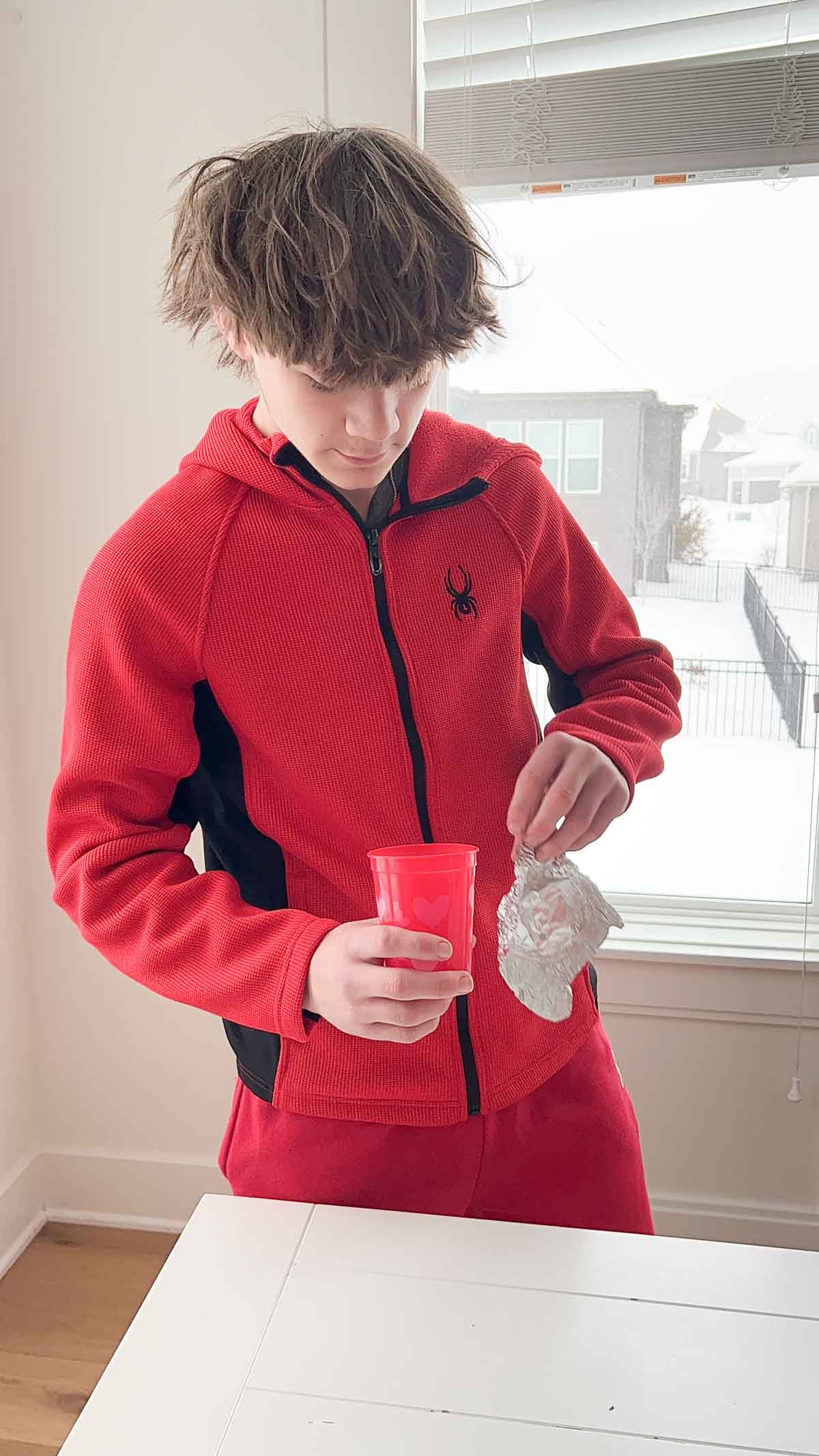 boy holding a cup standing next to a table