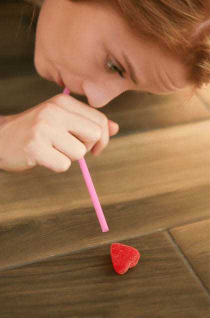woman blowing a candy heart with a straw
