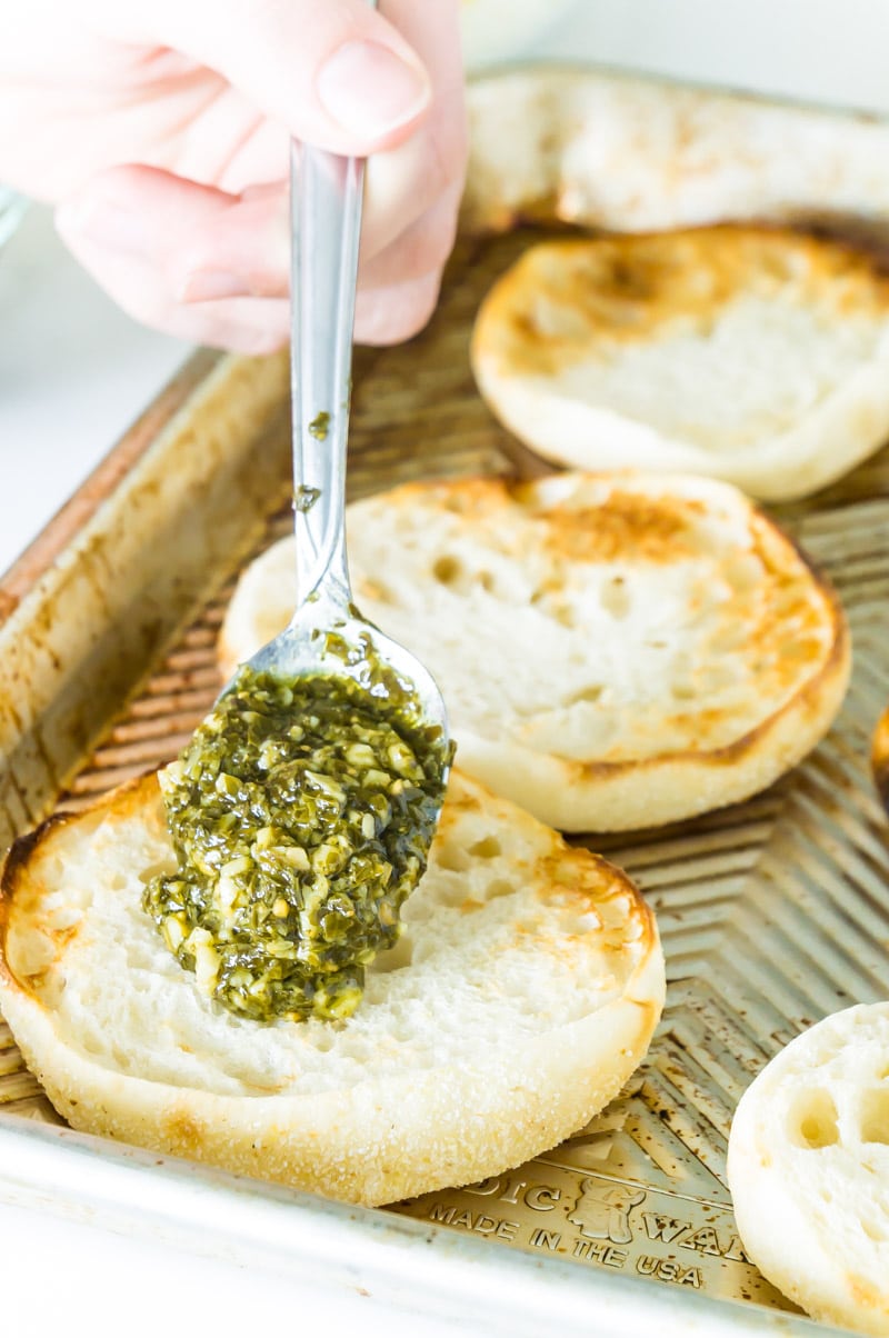 Layering pesto as the first step in the English muffin pizza recipe