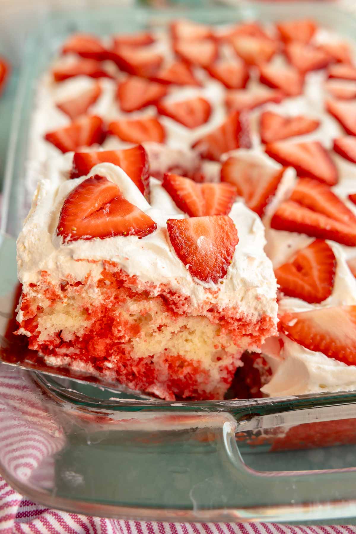 spatula removing a piece of strawberry poke cake from a pan