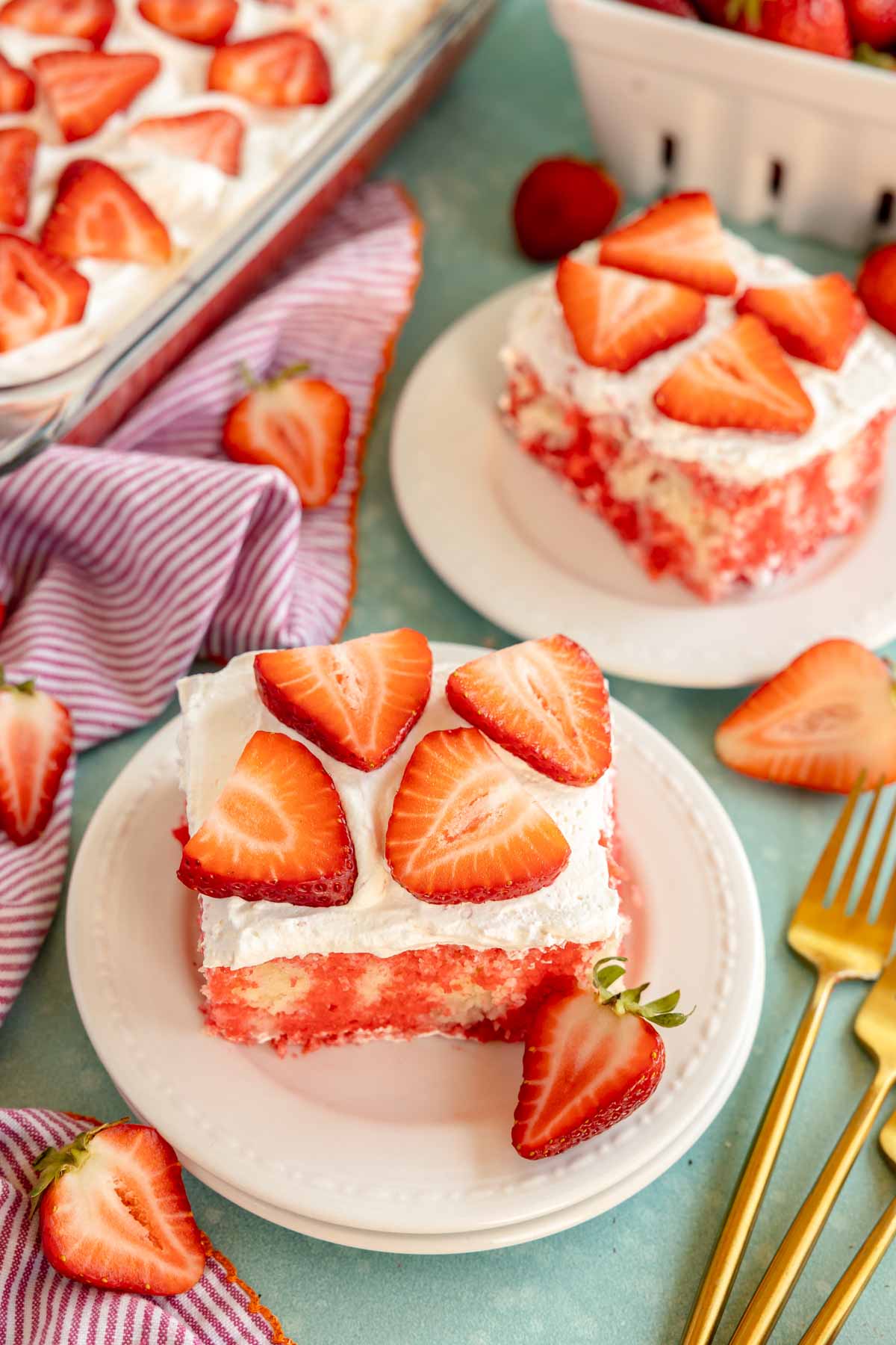 white plate with a slice of strawberry poke cake topped with strawberries