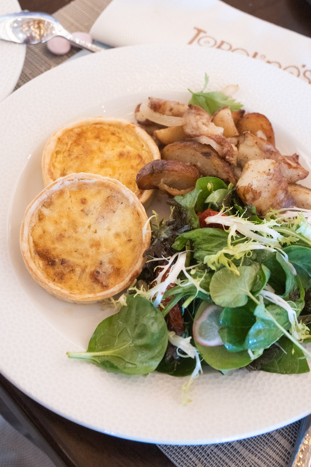 White plate with two quiche, greens, and potatoes