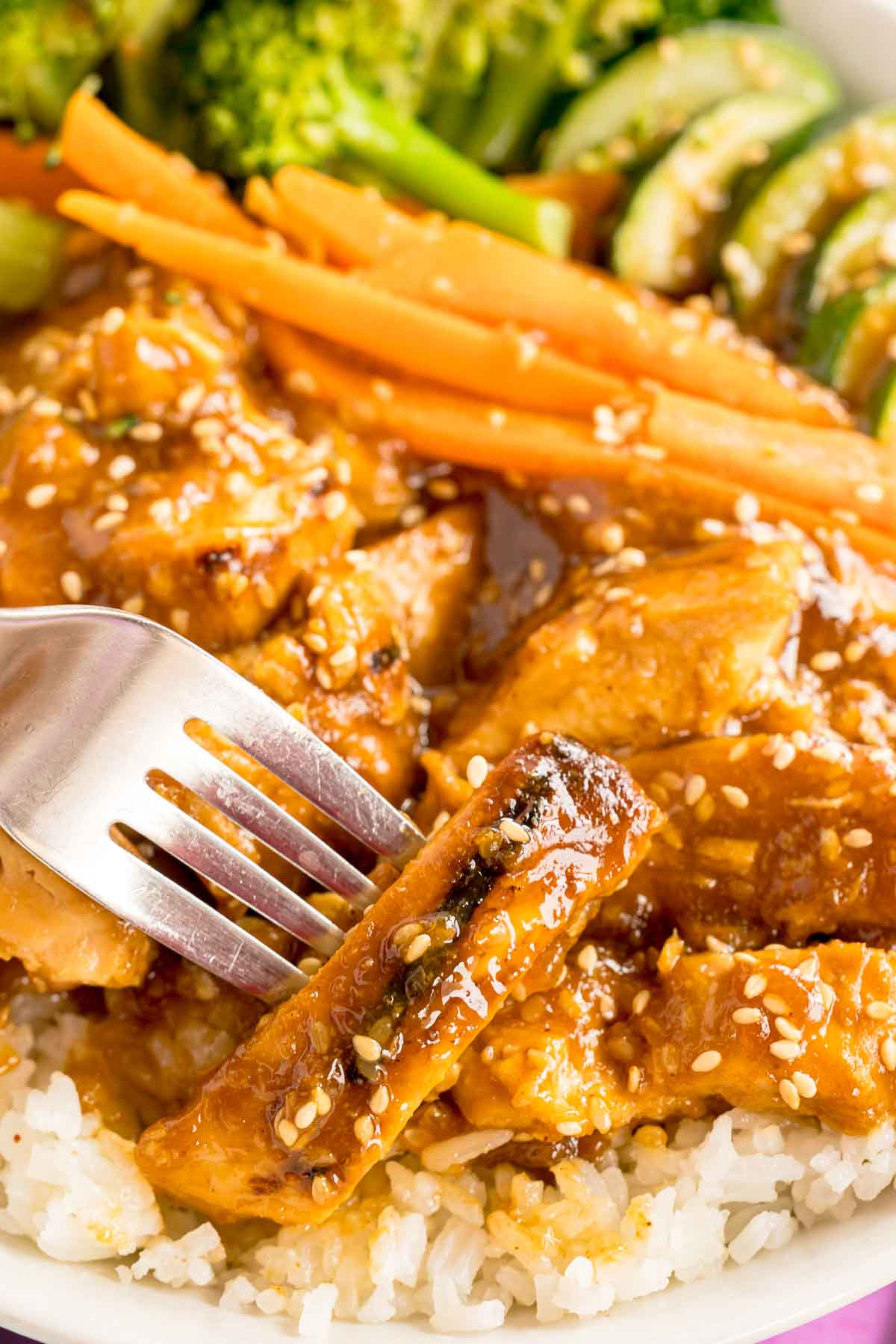 a fork stabbing a piece of teriyaki chicken on a plate