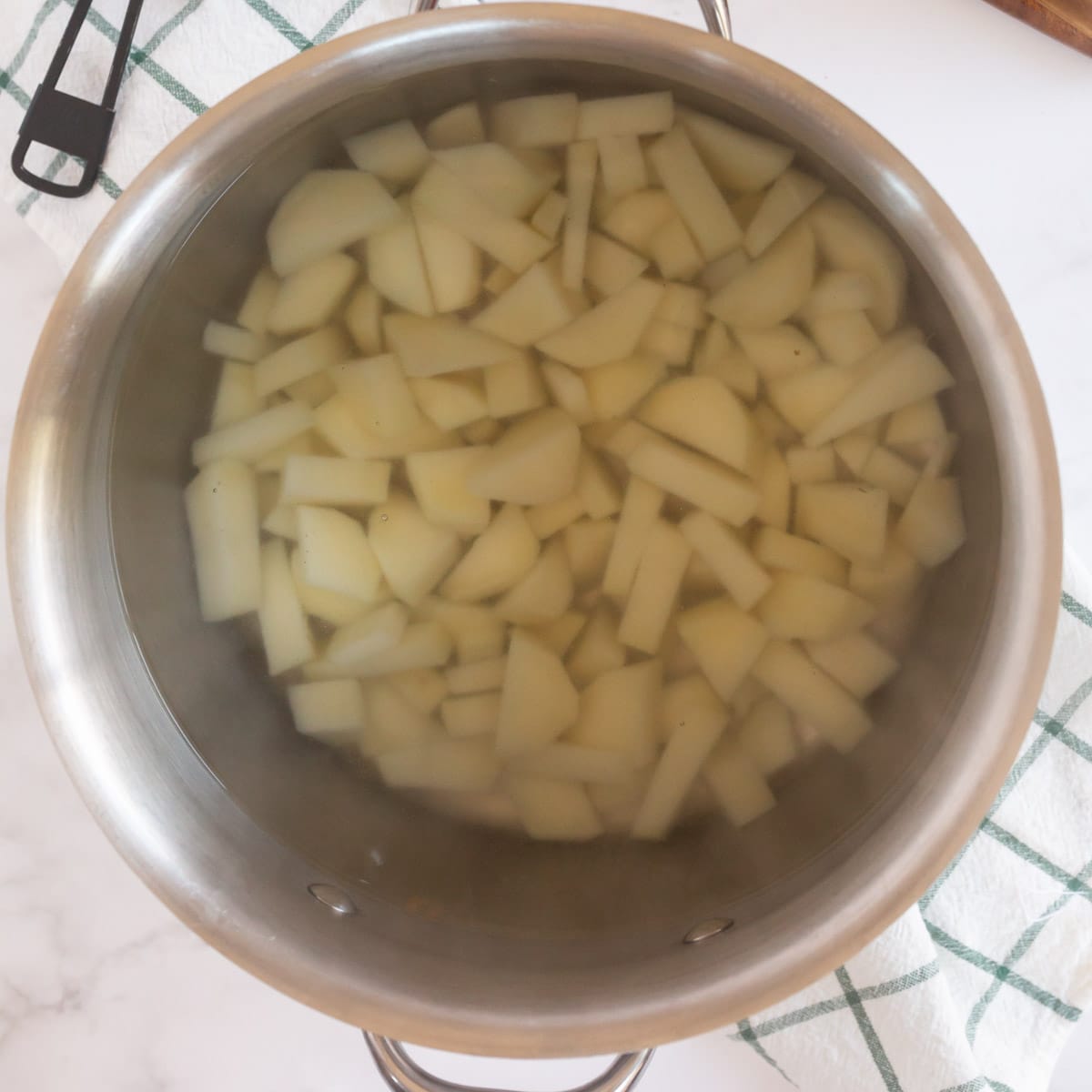 A metal pot with diced potatoes and water