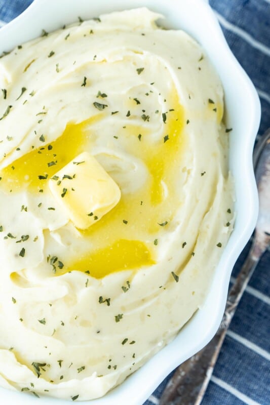 A bowl of mashed potatoes sprinkled with parsley and butter