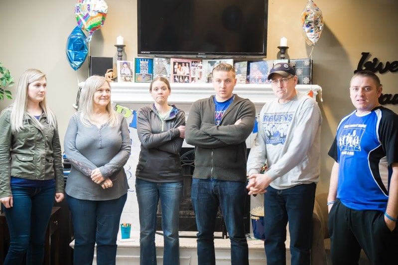 Group of adults standing in a line with birthday decorations on the wall behind them