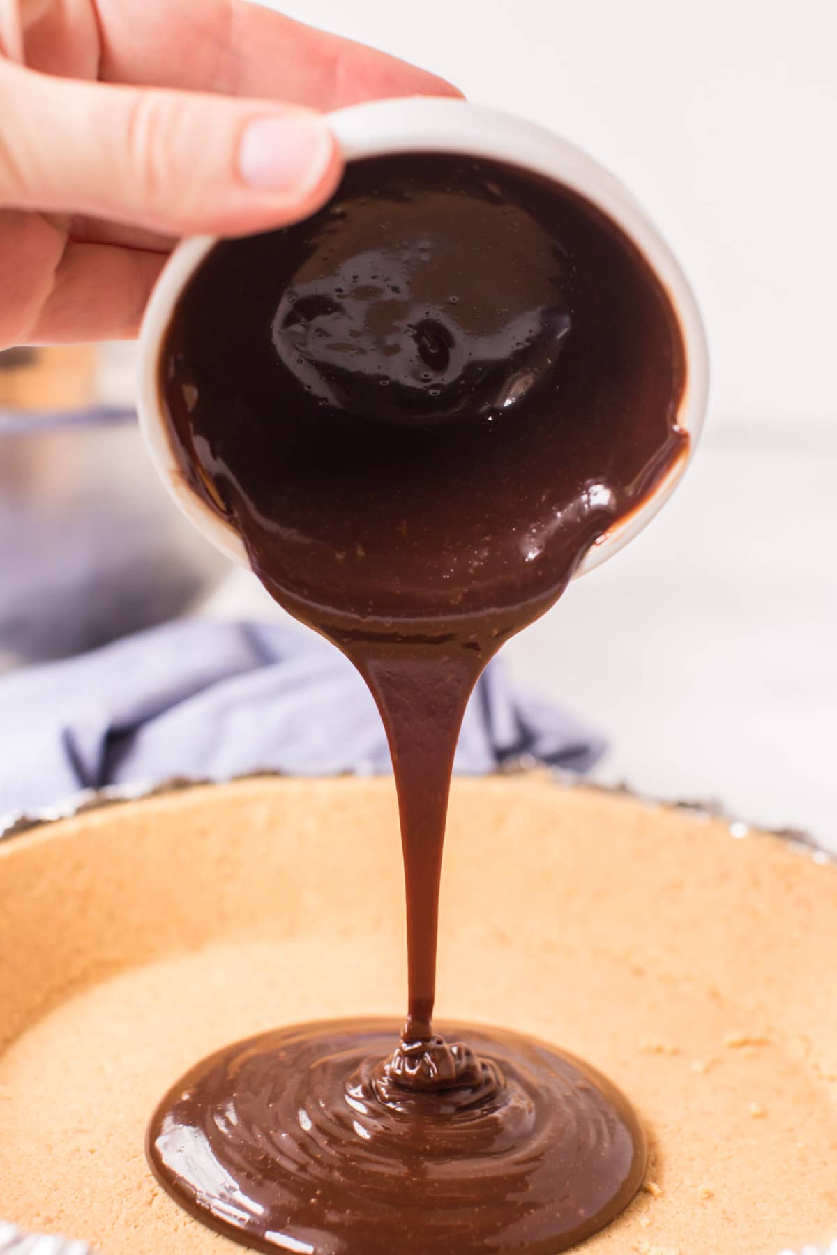 Pouring hot fudge into a graham cracker crust