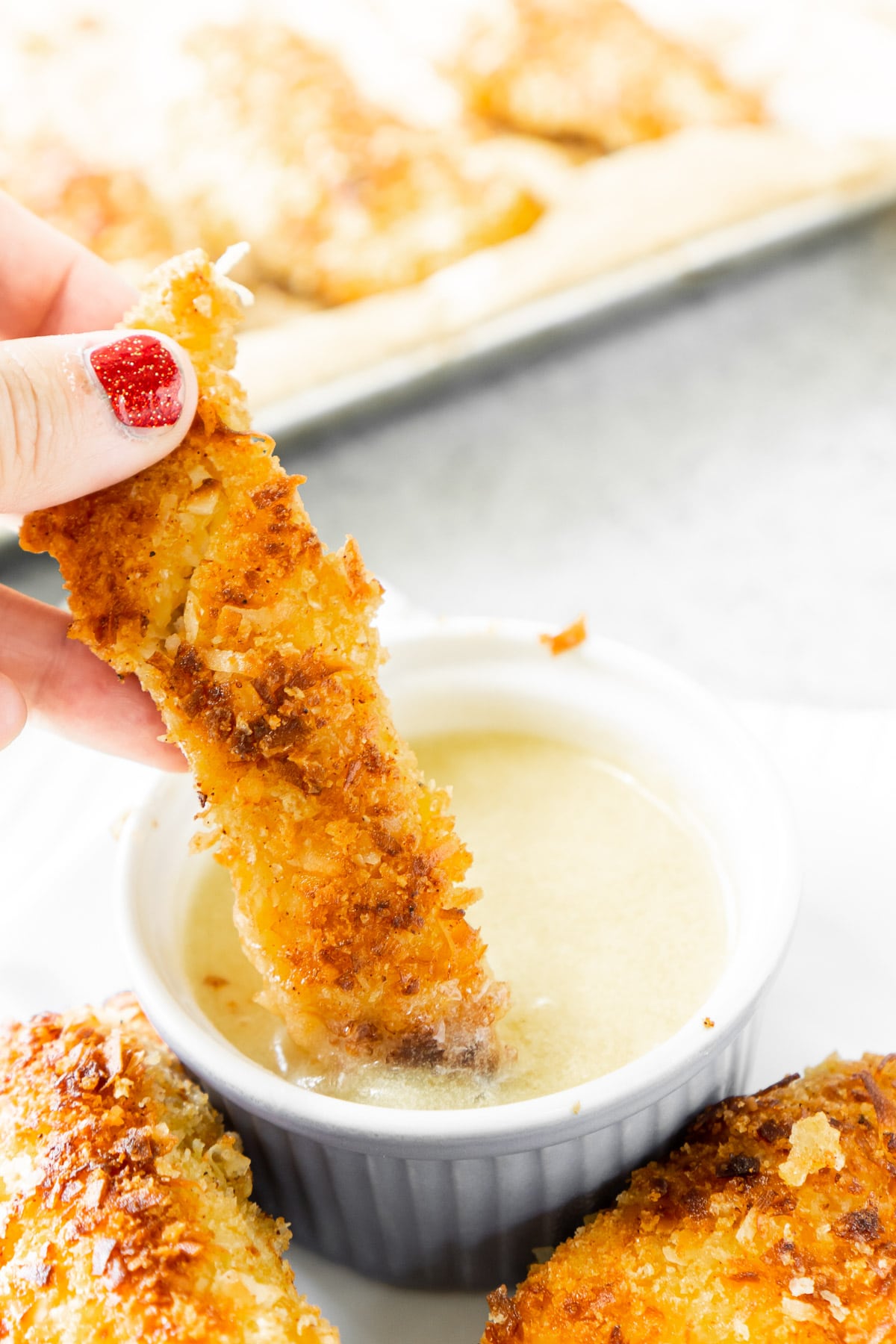 One coconut chicken tender being dipped into pina colada sauce