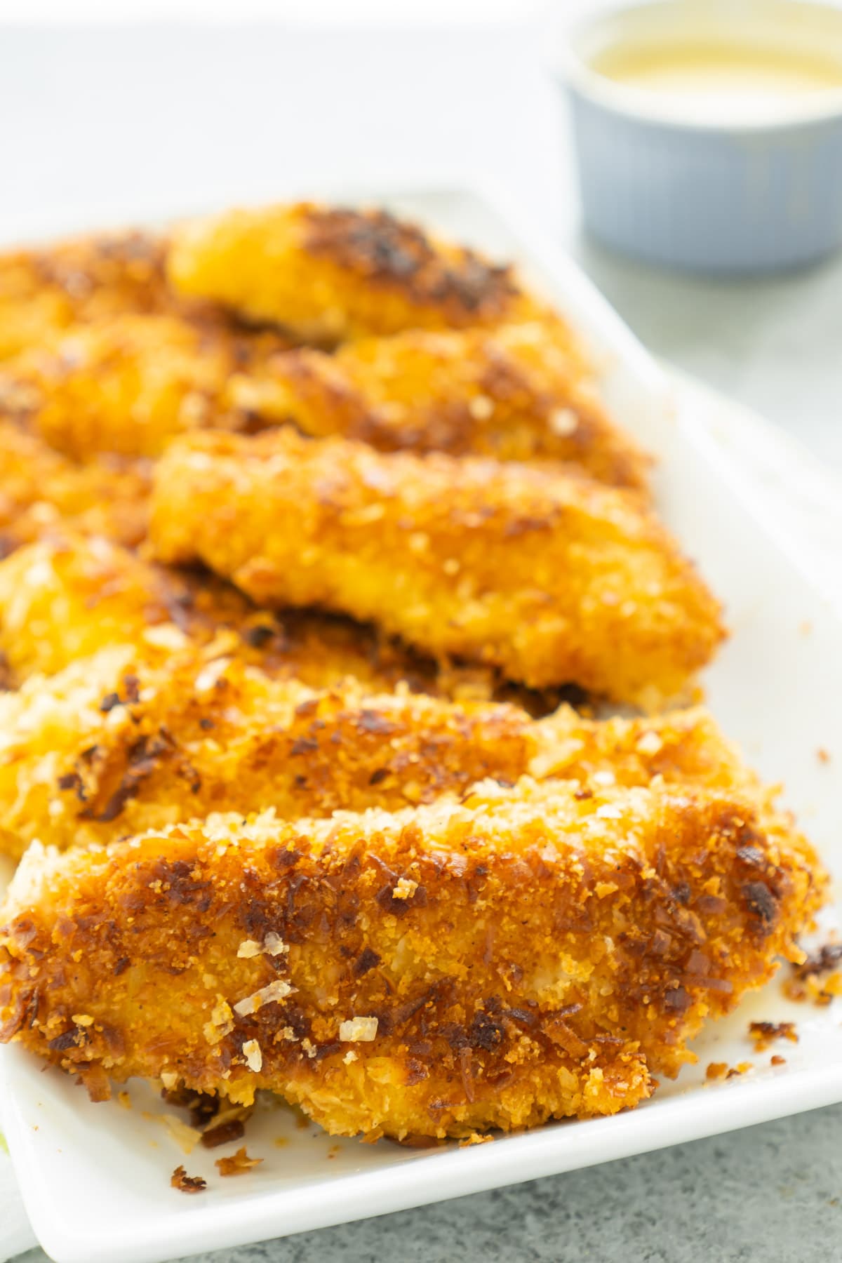 Pile of coconut chicken tenders on a white rectangle plate