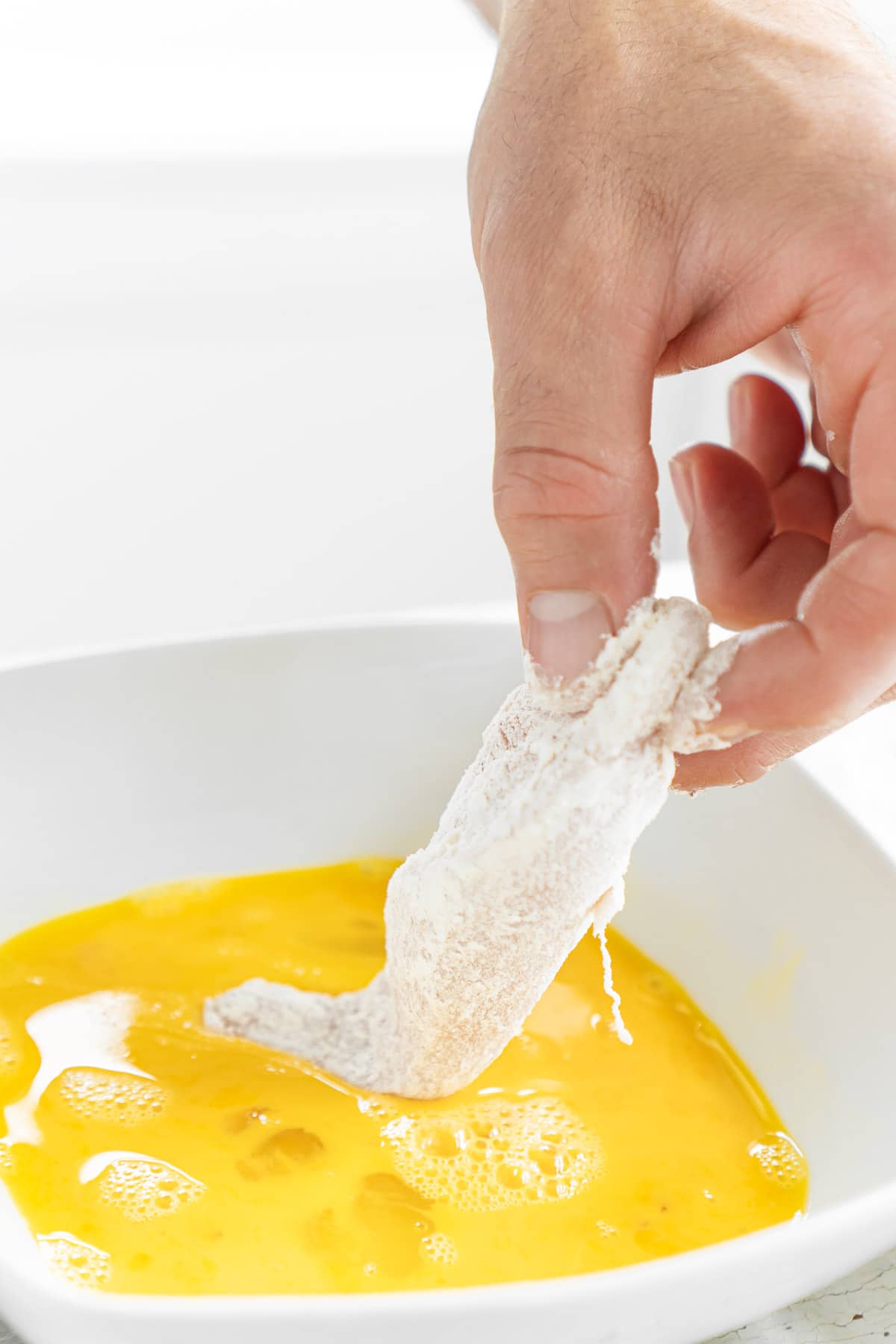 Man placing floured chicken tender into egg in a bowl