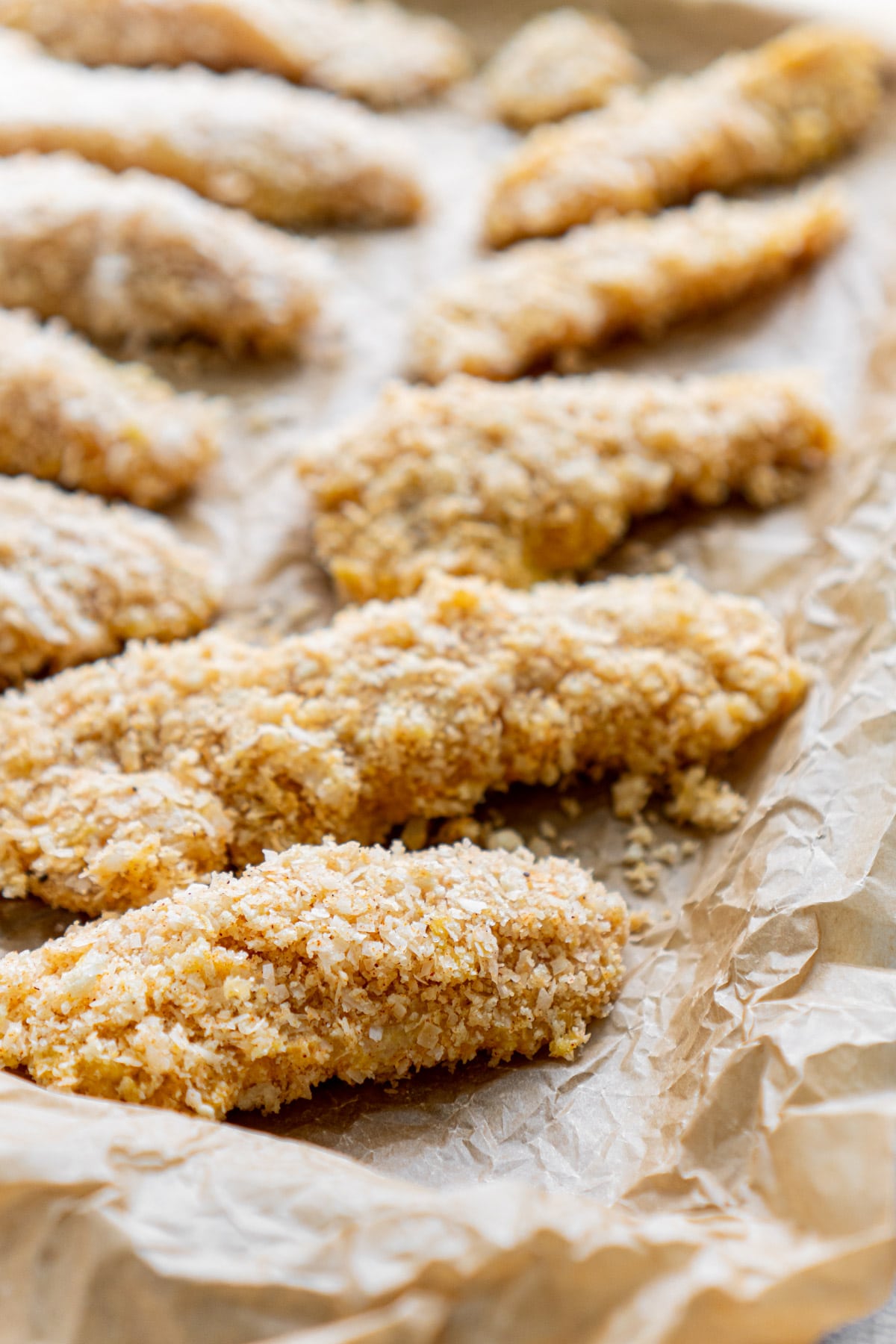 Coconut chicken tenders in a line on a parchment lined baking sheet