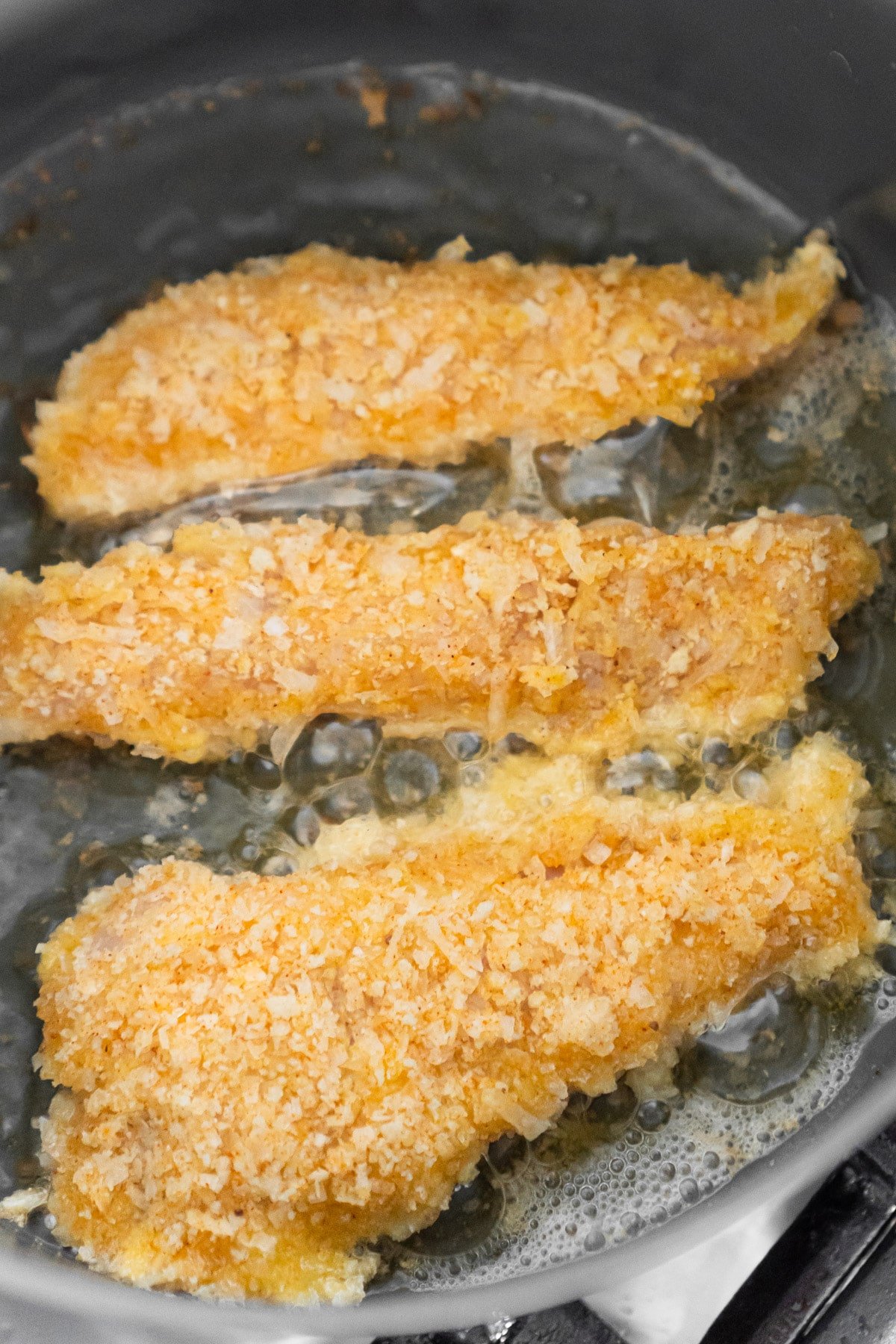 Coconut chicken tenders in coconut oil pan frying