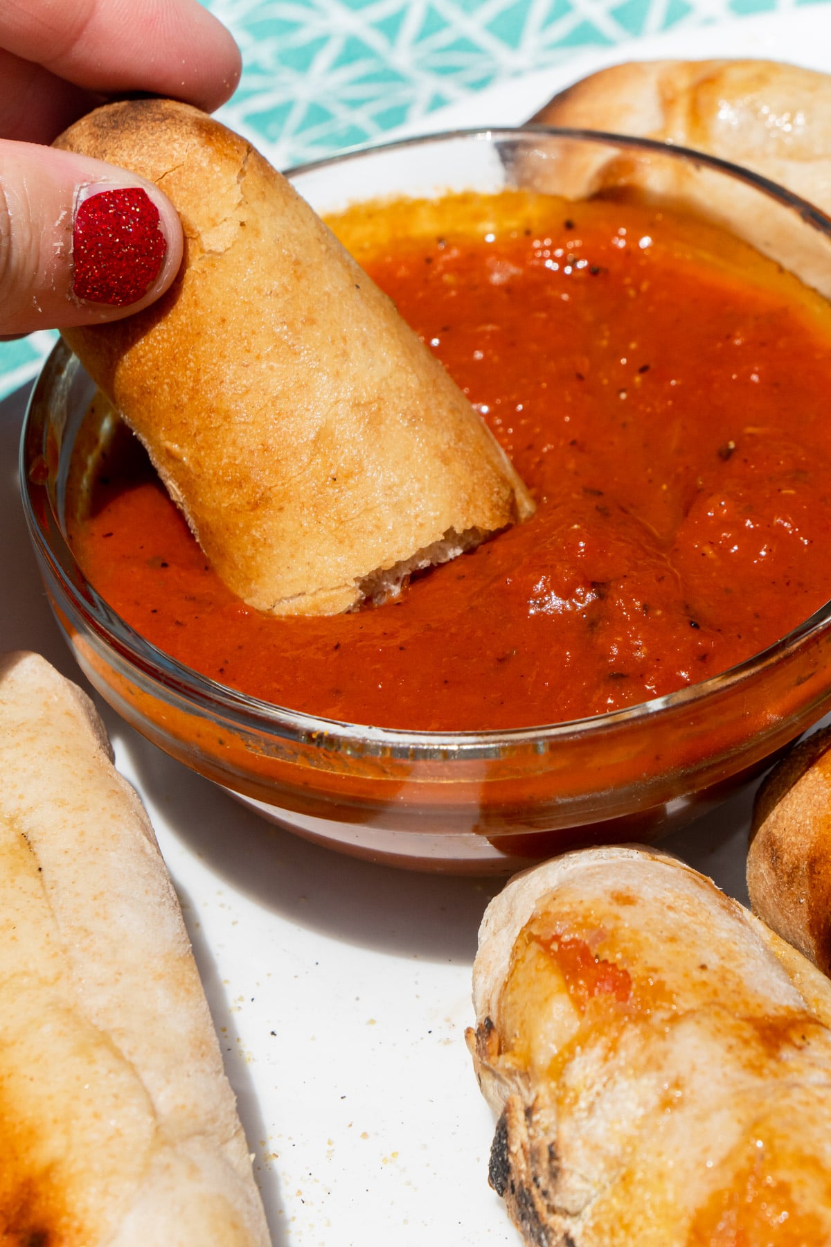 Woman's hand dipping pepperoni rolls into pizza sauce