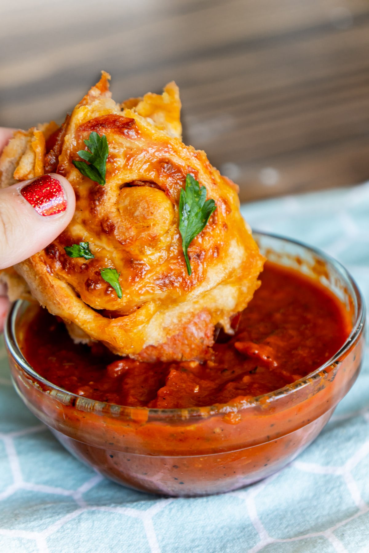 Woman's hand dipping a pepperoni roll into glass bowl of pizza sauce