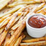 A pile of air fryer fries with a small white cup of ketchup