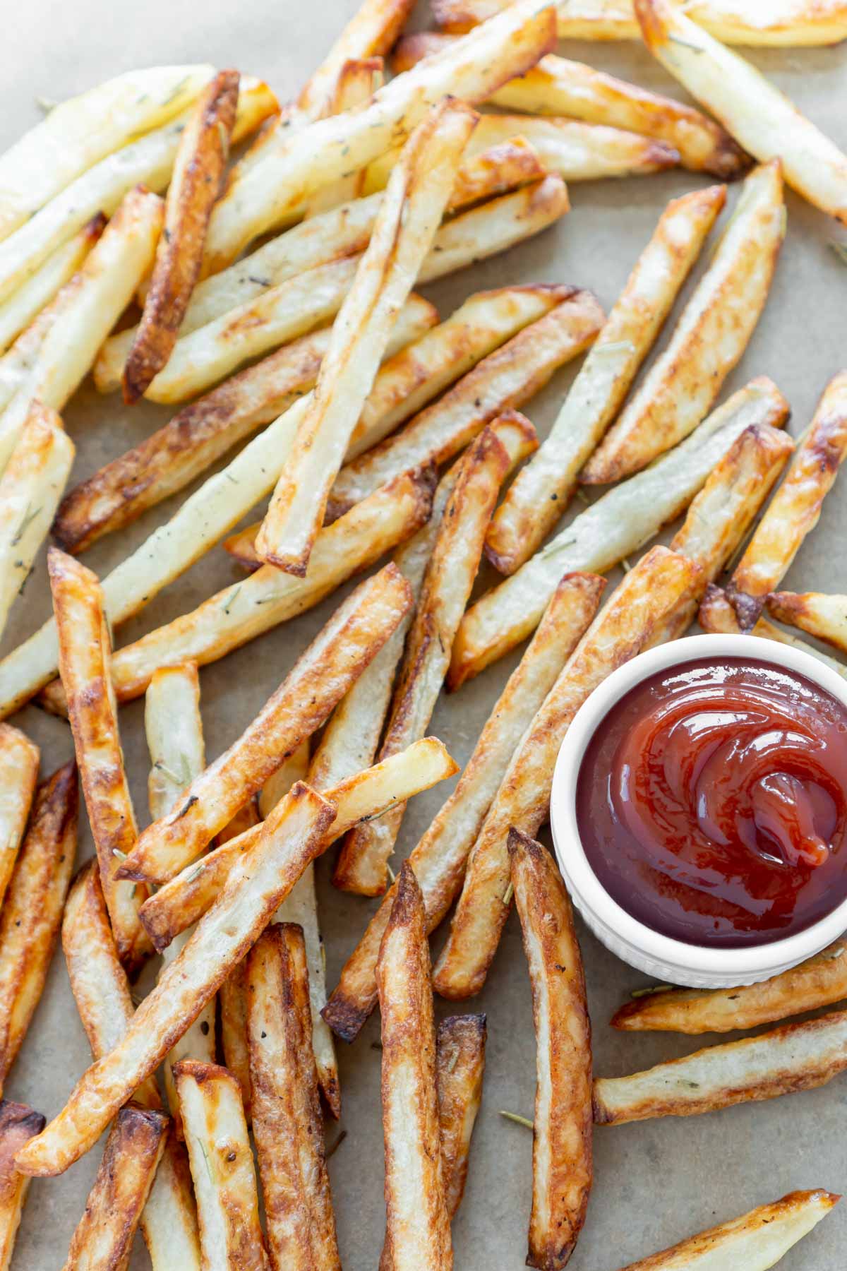 An overhead shot of a bunch of crispy french fries with a white container of ketchup