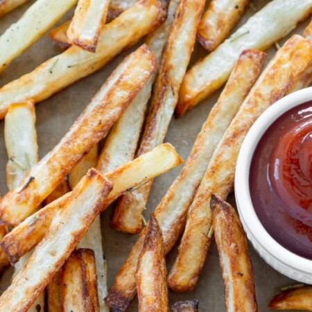 A horizontal photo of air fryer french fries and a white bowl of ketchup