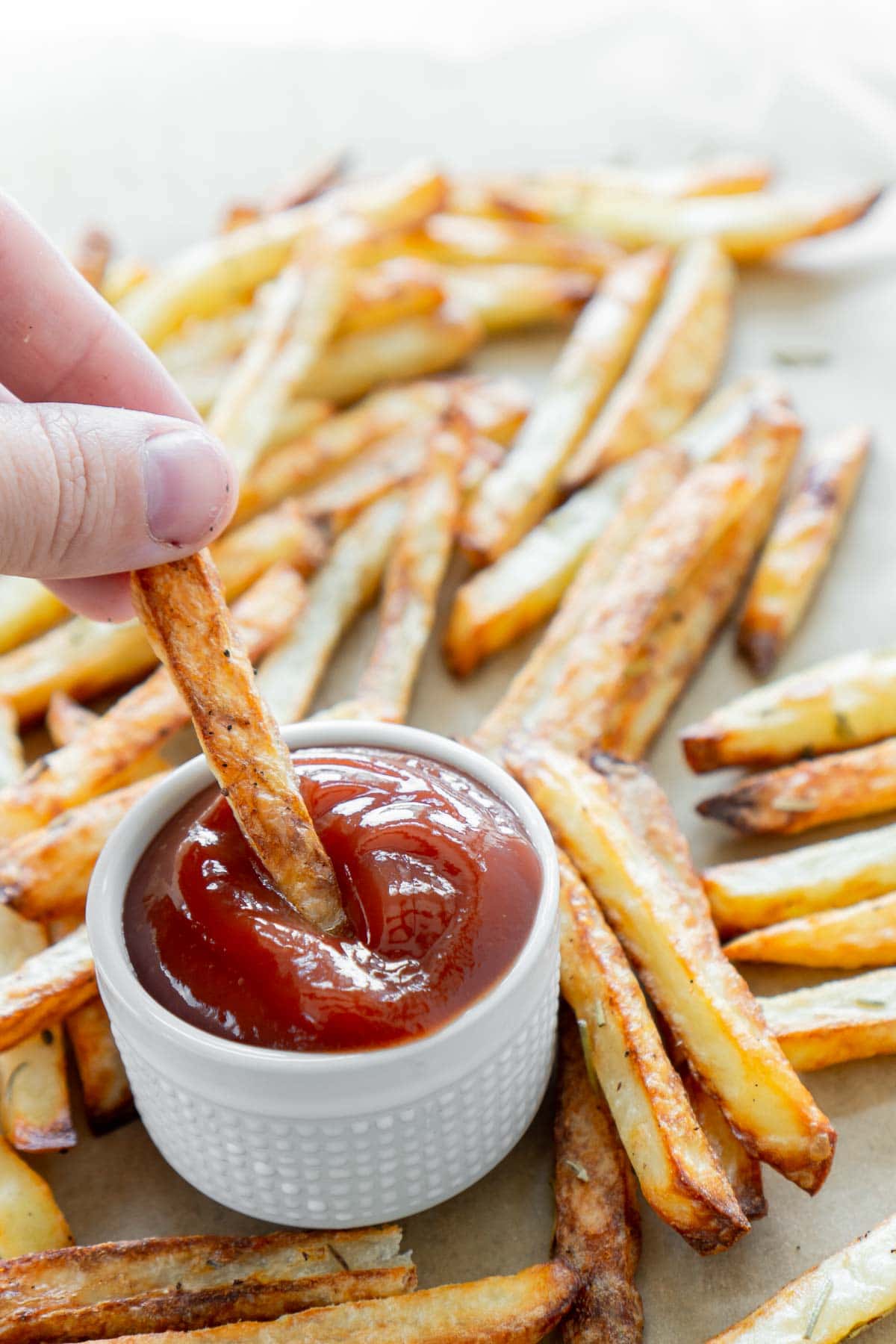 Woman's hand dipping a french fry in ketchup with a plate of air fryer fries