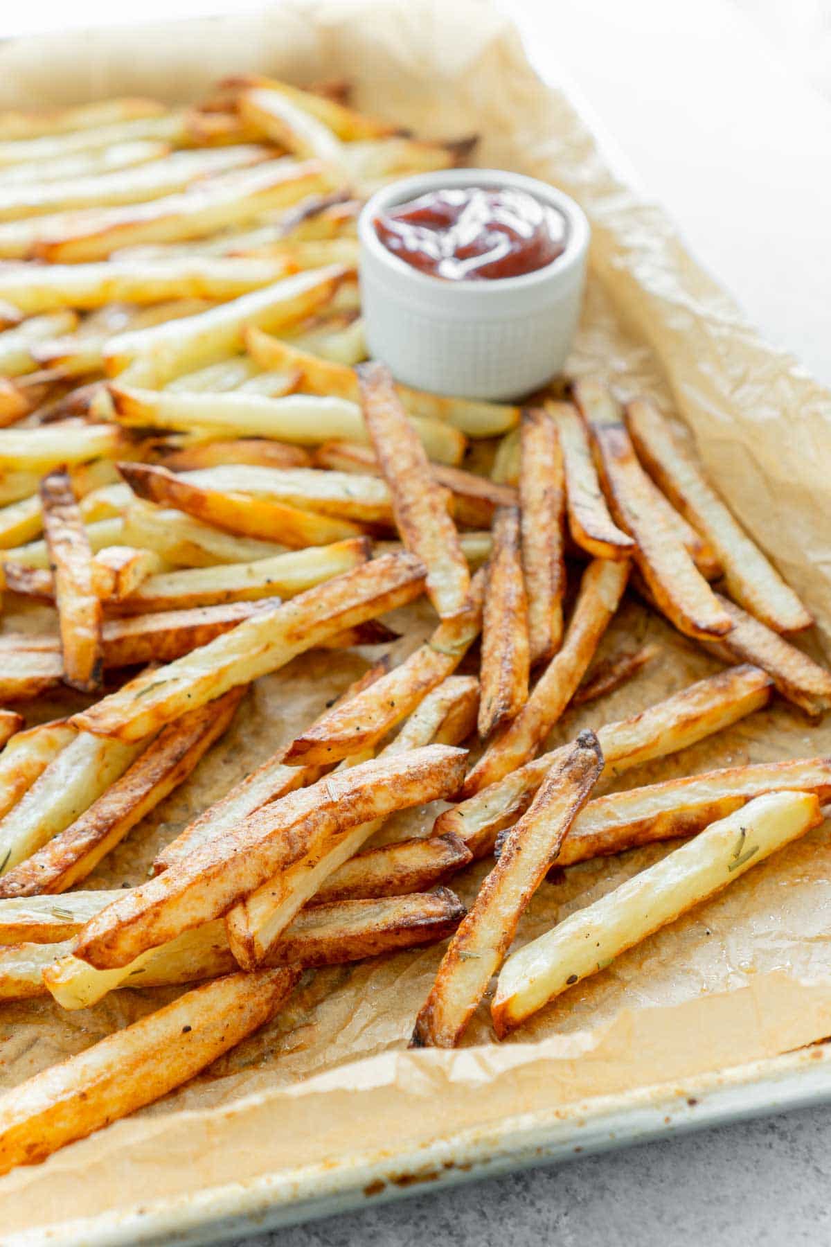 Pile of homemade fryer french fries on a baking sheet with parchment paper