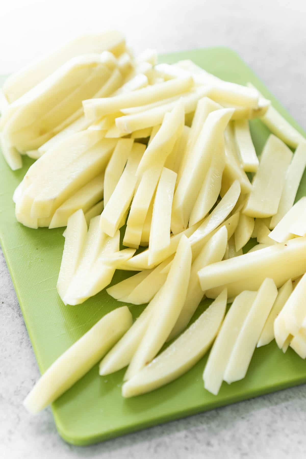 A pile of potatoes cut into french fries on a green cutting board