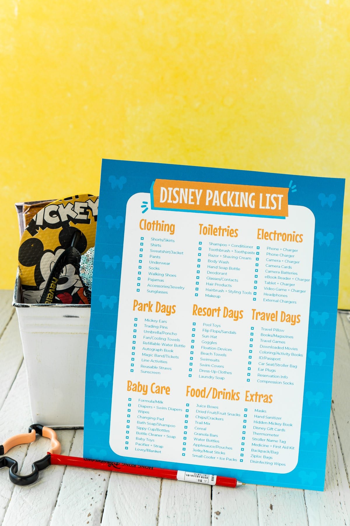 Disney packing list in front of a bucket full of Disney items with a yellow background