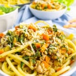 A close up view of a white bowl with ground turkey pasta and a blue napkin