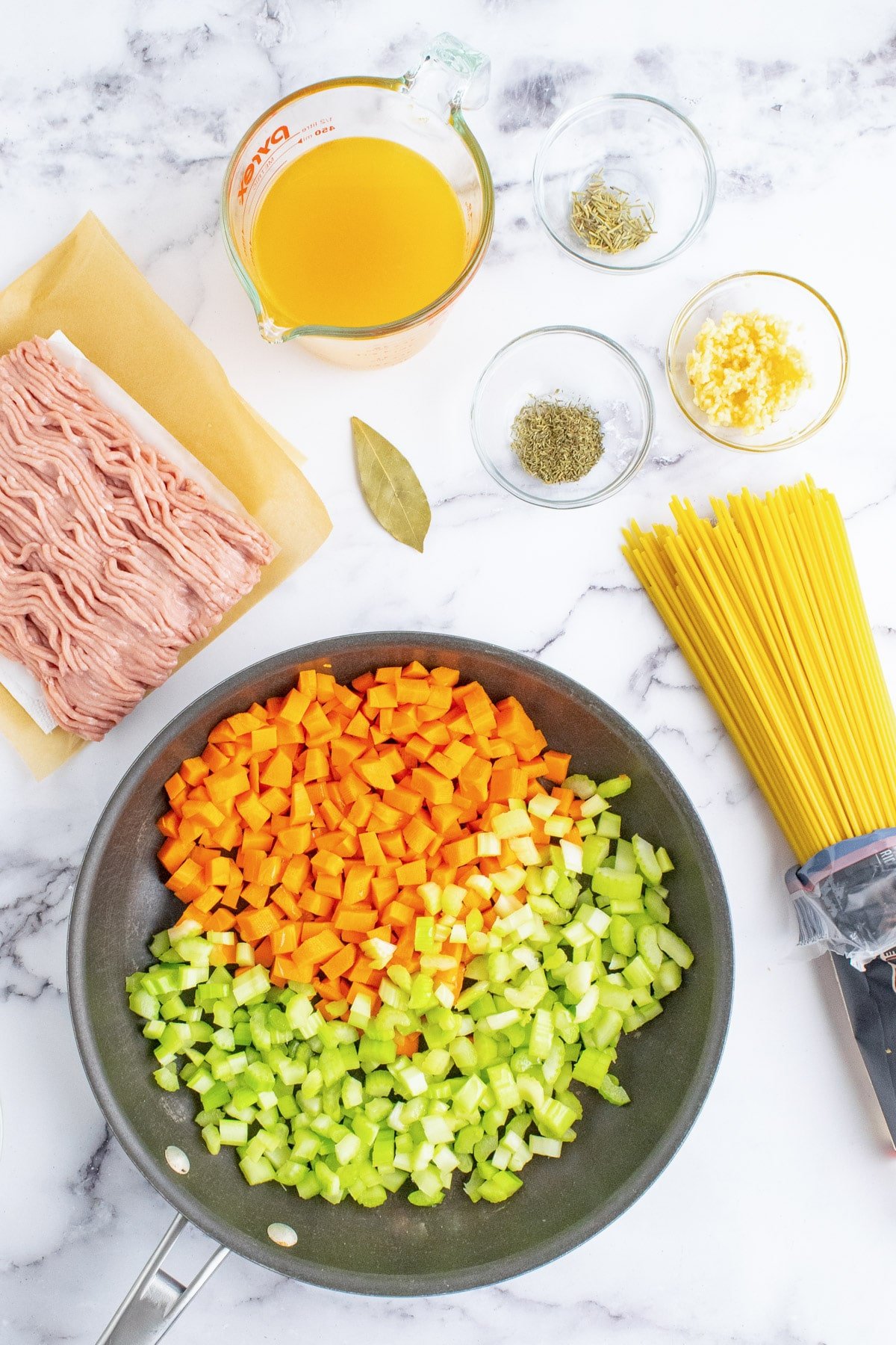 Celery and carrots in a pan with other ingredients for ground turkey pasta around it