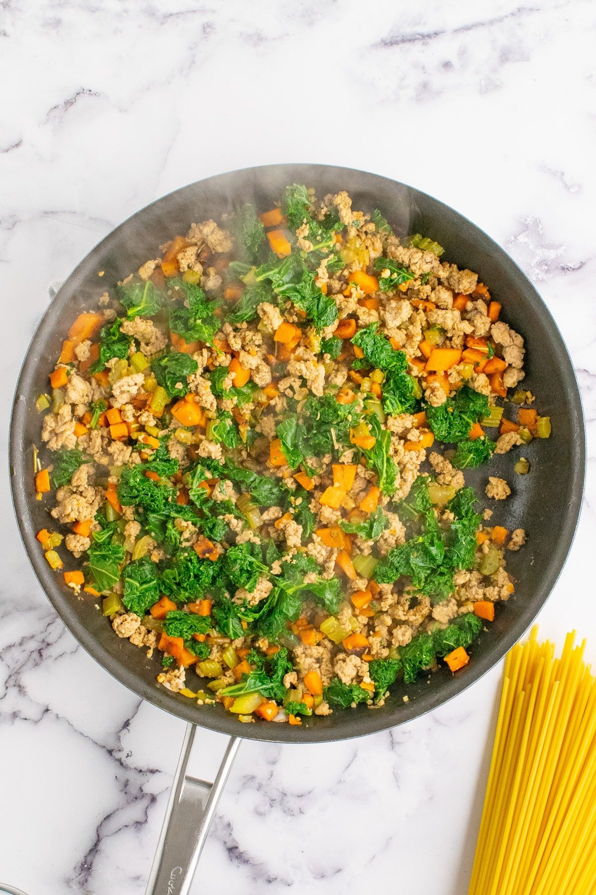 Carrots, celery, and kale in a pan with pasta on the side