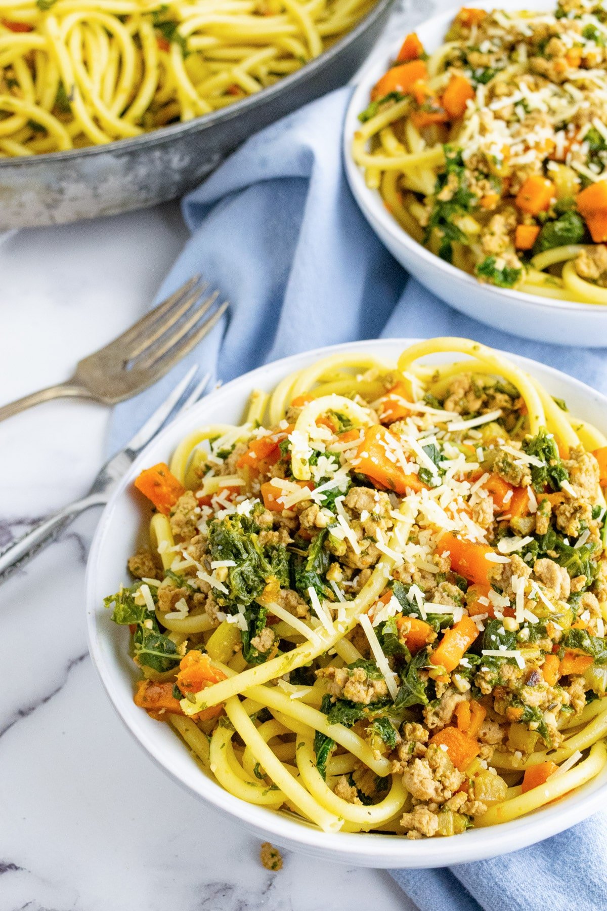 Two bowls of ground turkey pasta with veggies and a blue napkin