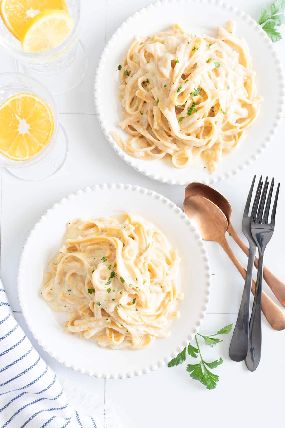 Two plates of Instant Pot fettuccine alfredo on a white plates with silverware and pieces of parsley