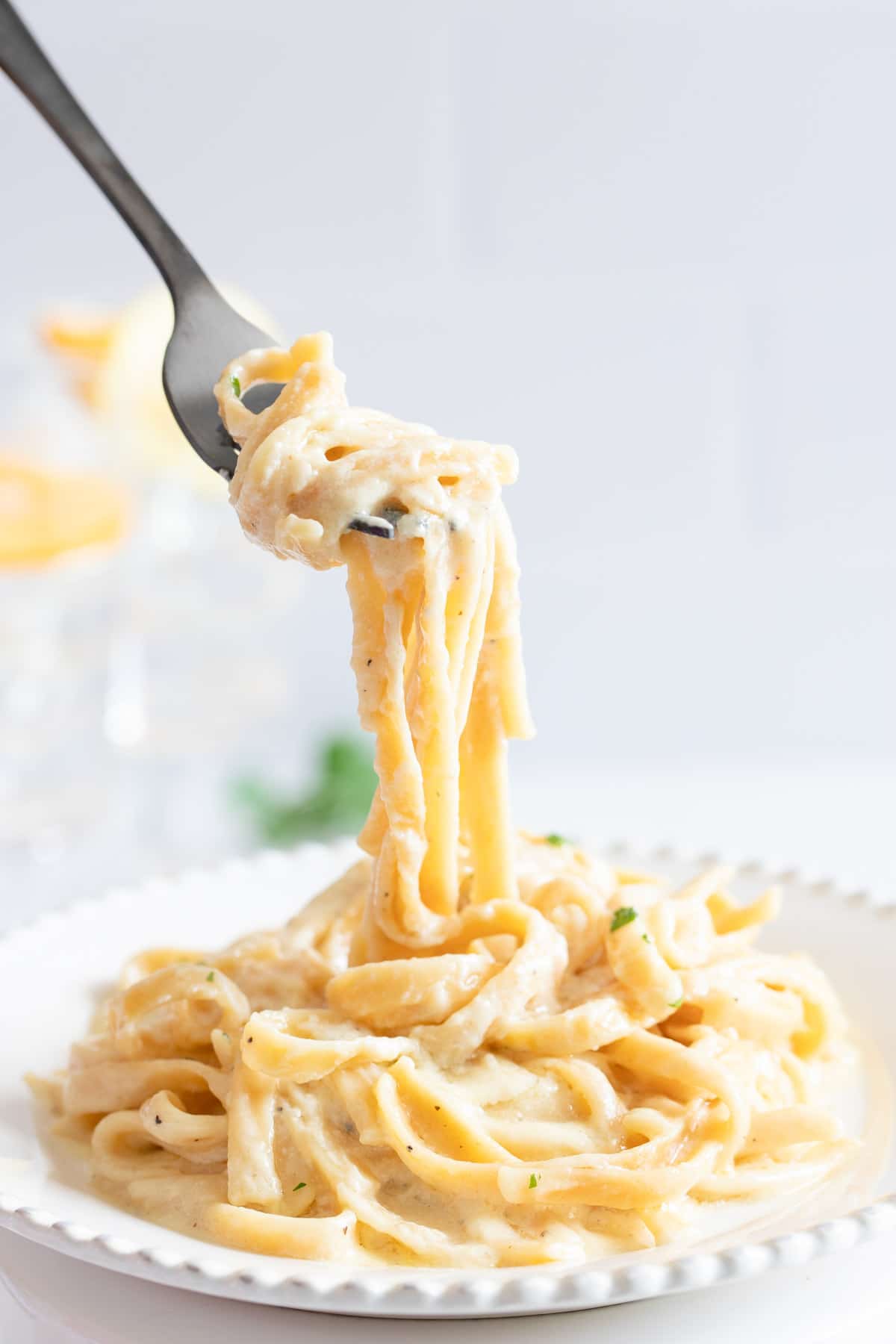 A fork with a bite of fettuccine alfredo held above a plate full of pasta