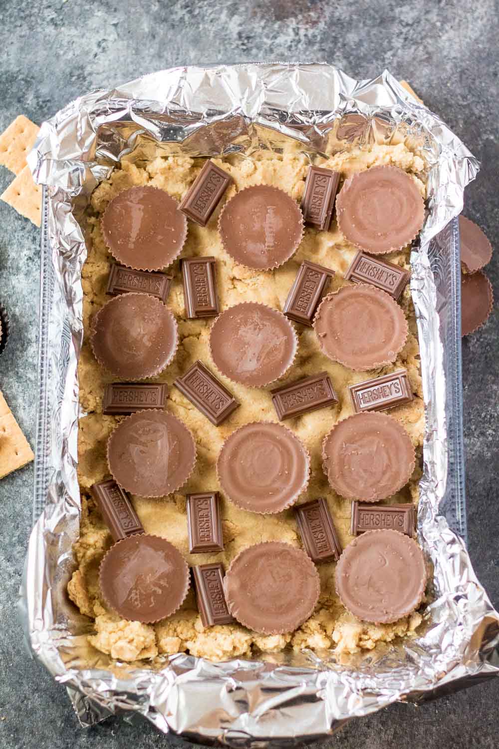 Peanut butter cup and Hershey chocolate pieces on top of a smore bar crust in a baking dish