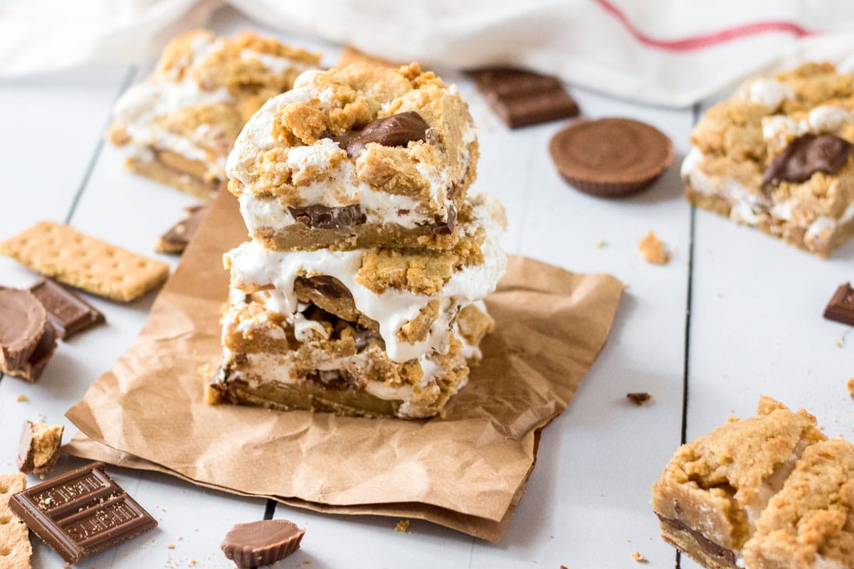 Two smore bars stacked on a brown napkin with peanut butter cups and chocolate bars around