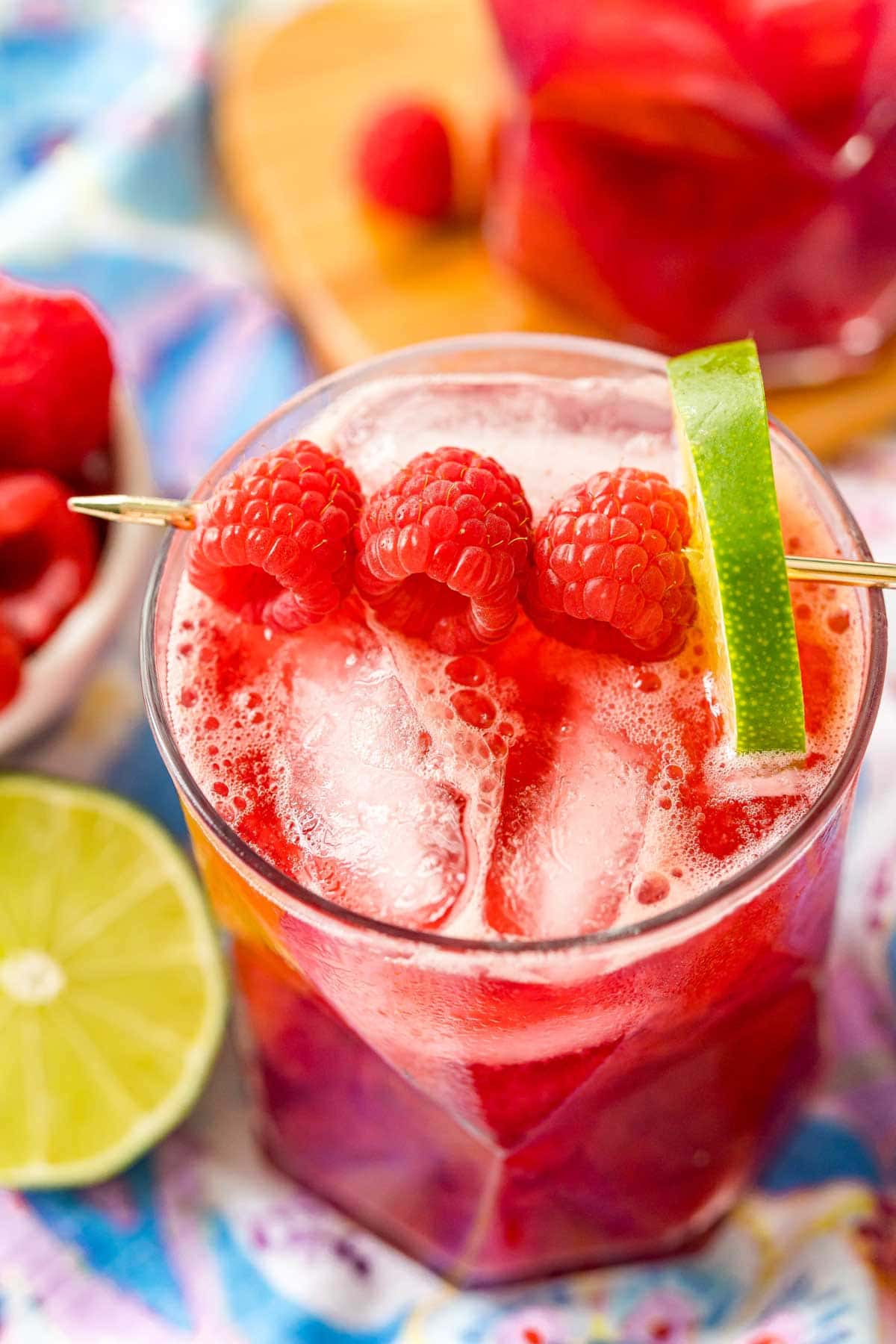 A glass of summer punch with three raspberries and a lime wedge on top