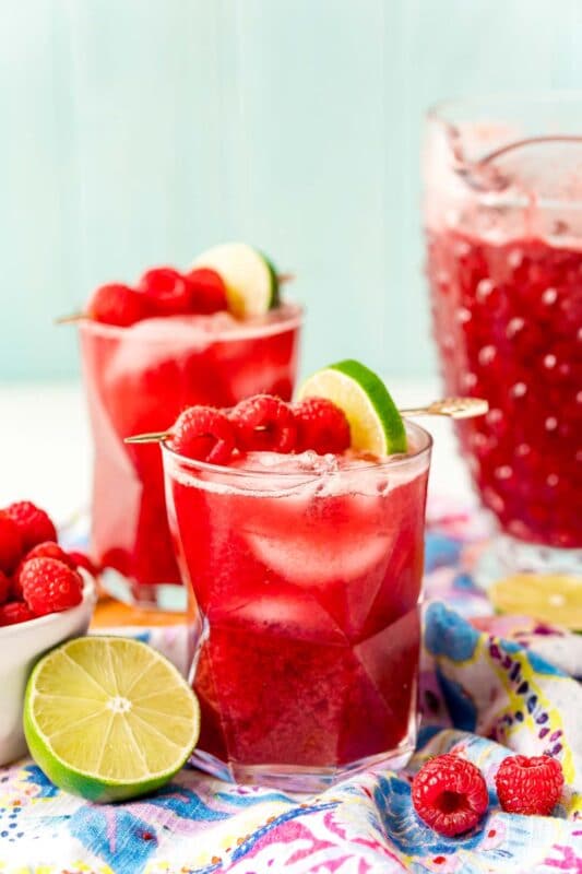 Two glasses of red raspberry punch with a pitcher of punch in the background