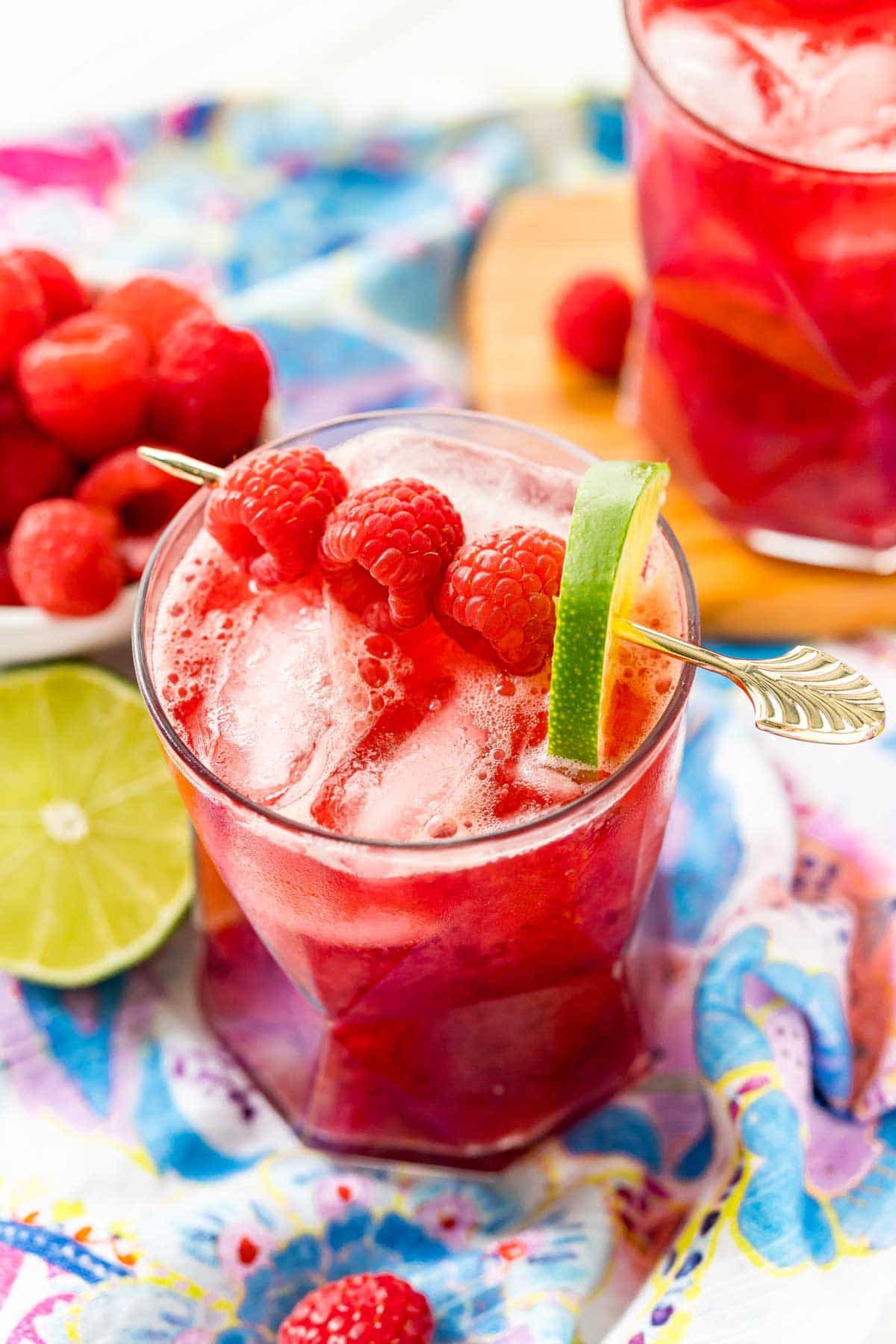 A glass or raspberry punch with lime garnish and a colorful napkin in the background