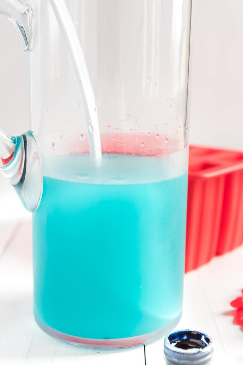 A glass pitcher with blue lemonade inside